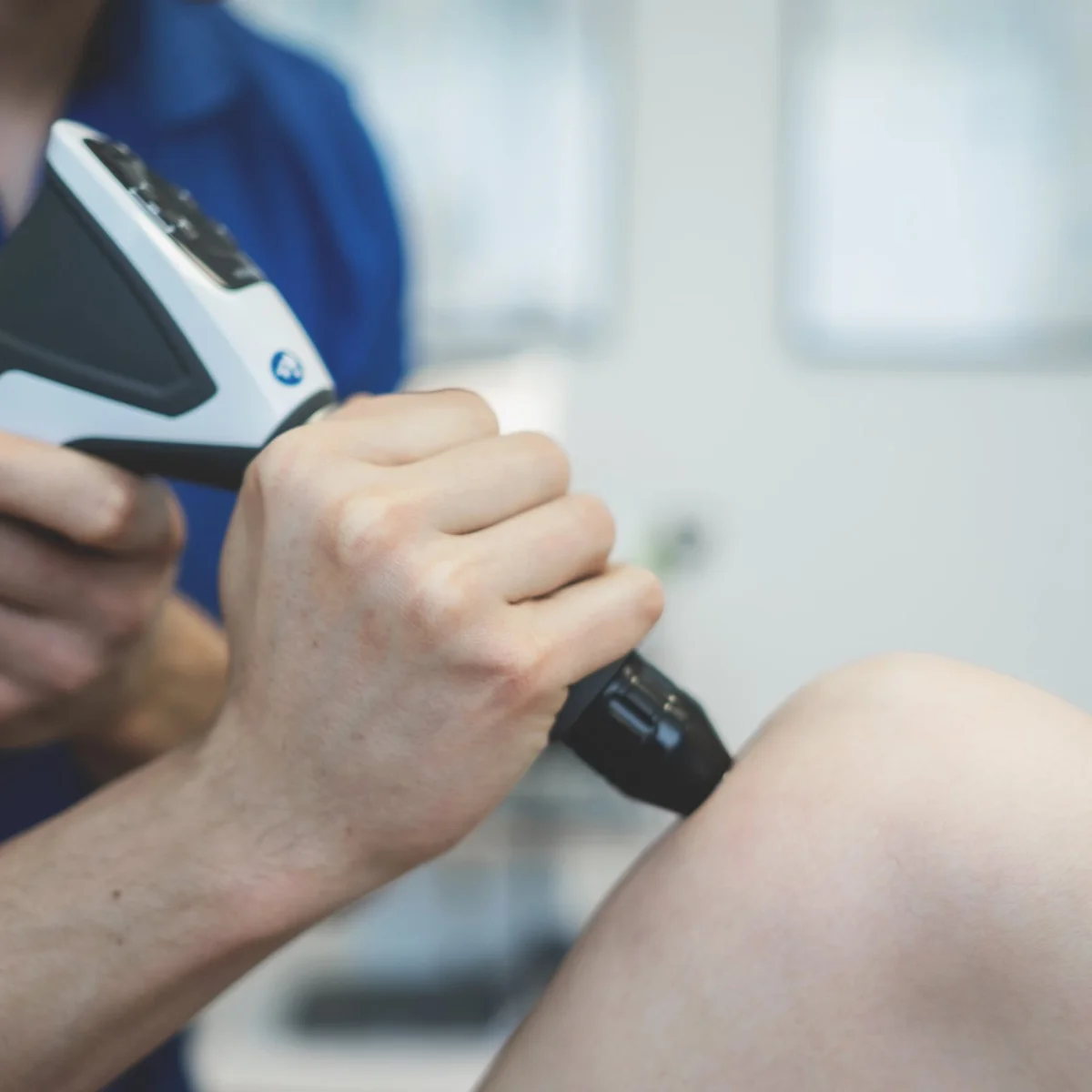 Fysiotherapeut behandelt de knie van een patiënt met een shockwave-apparaat